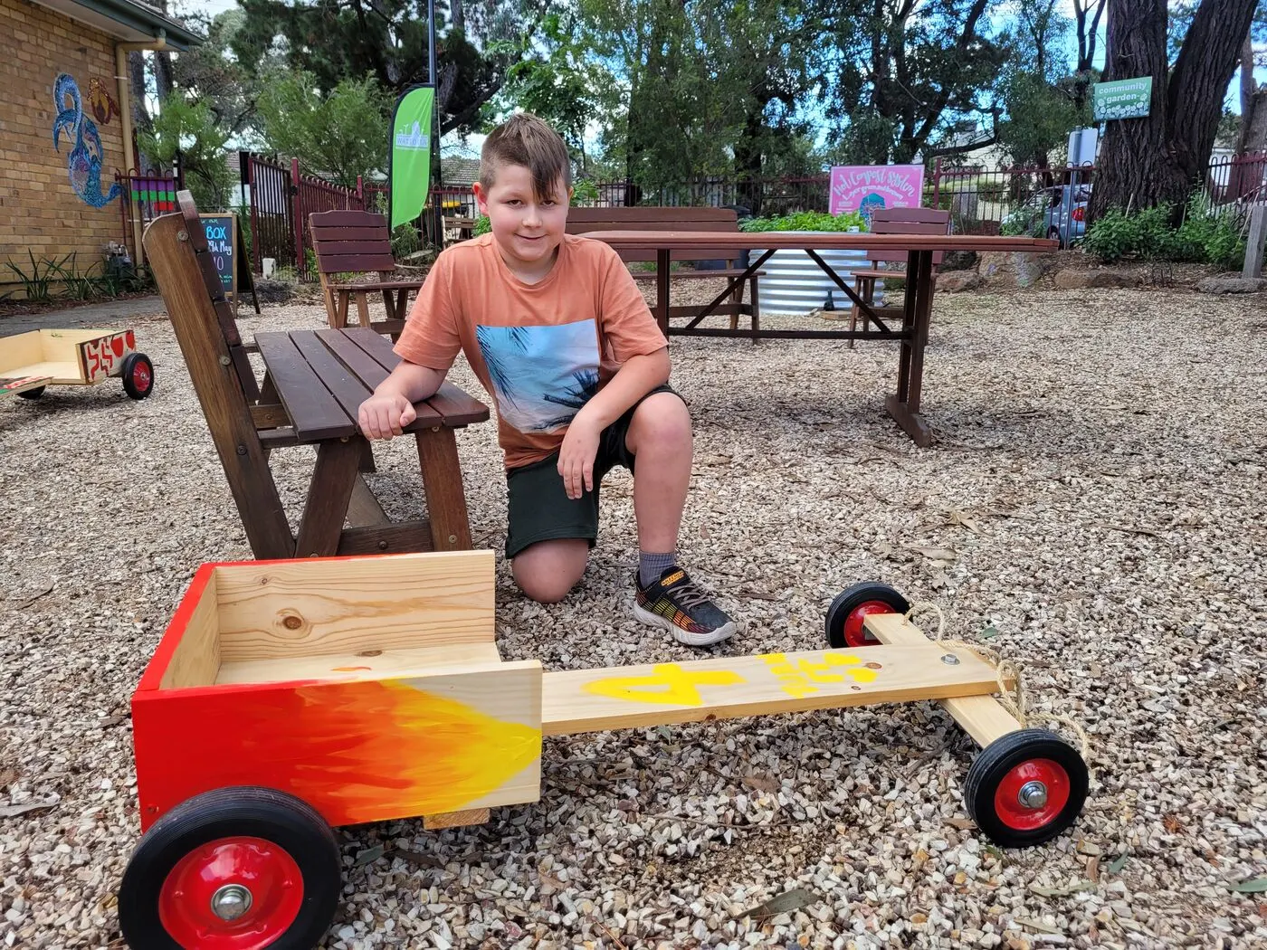 A child sitting on a finished billy cart outside on the gravel