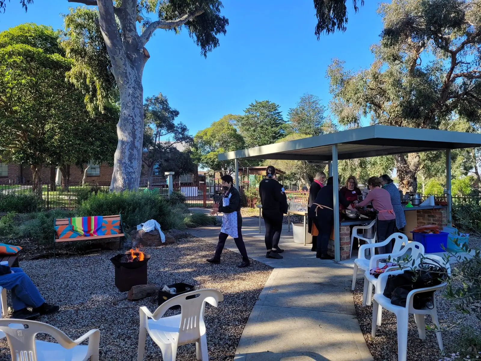 The outdoor courtyard under a shade sail, with a concrete path, chairs and gum trees beyond