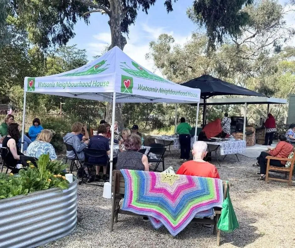 People sitting together under marquees in the garden on a sunny day, beside a raised planter