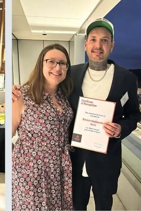 Two people standing together at the awards night, one holding a framed certificate of recognition