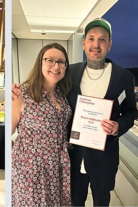 Two people standing together at the awards night, one holding a framed certificate of recognition