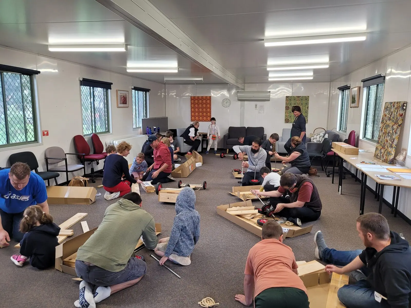 A room full of people sitting on the floor and at tables working on a shared craft project