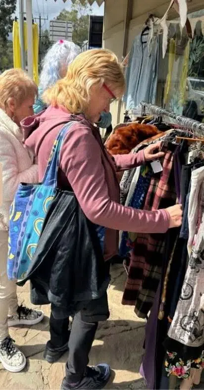 Two people looking through a rack of clothes on the footpath outside an op shop