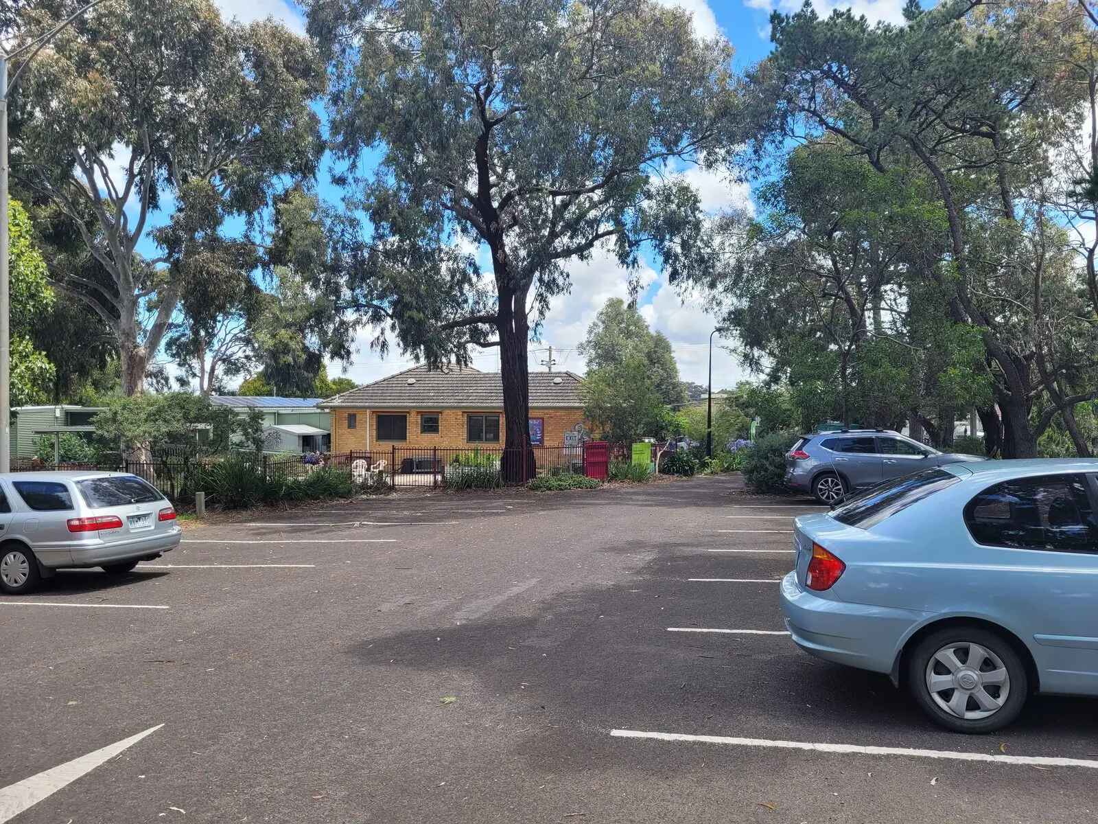 The off-street car park beside the House, marked bays under gum trees with the building at the far end