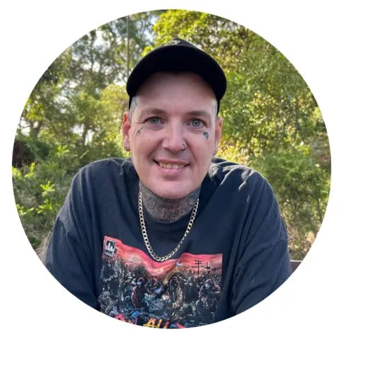 Shannon Boyd smiling, wearing a cap, with greenery behind